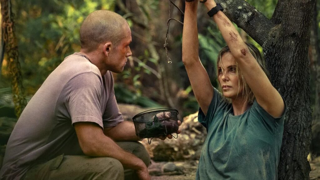 ‘Apex’ Review: Charlize Theron Netflix Thriller Avoids Rock Bottom, but Barely Production still from Apex showing Charlize Theron tied to a tree and Taron Egerton with a shaved head terrorizing her.