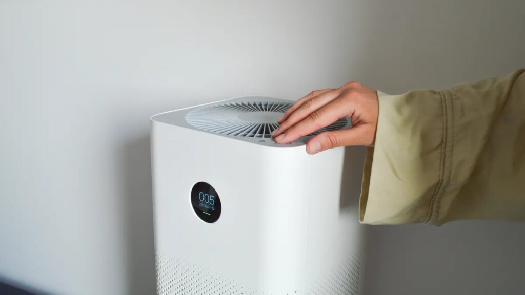 Your Air Purifier Could Spit Pollutants Back Into the Air if You Make This One Mistake A hand touching the top of a white air purifier.