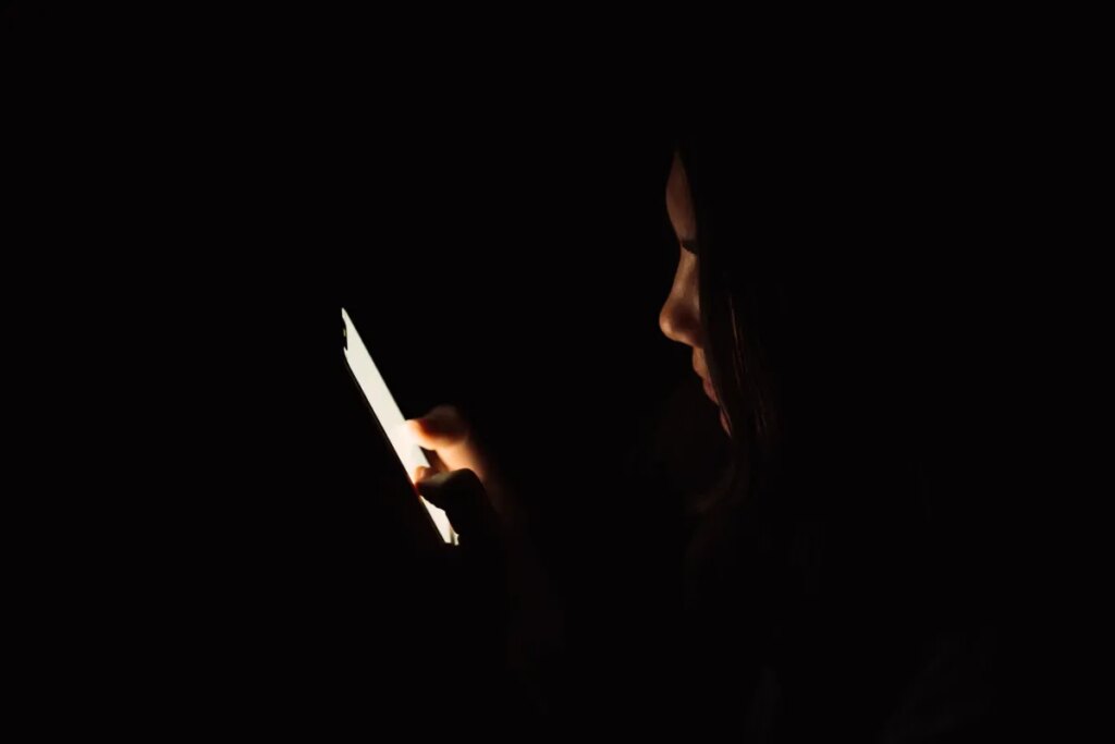 These special phone and app features can help protect you from spyware Lady looking at smartphone in dark room.