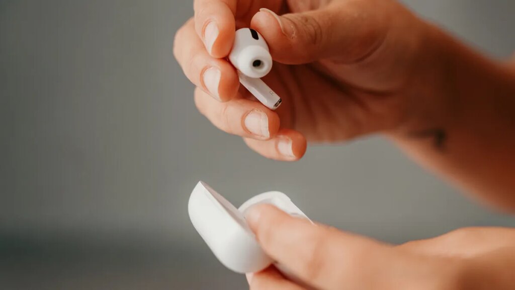 Apple Is Reportedly Planning AirPods With Cameras for 2027 Two hands holding one AirPod and an AirPod case
