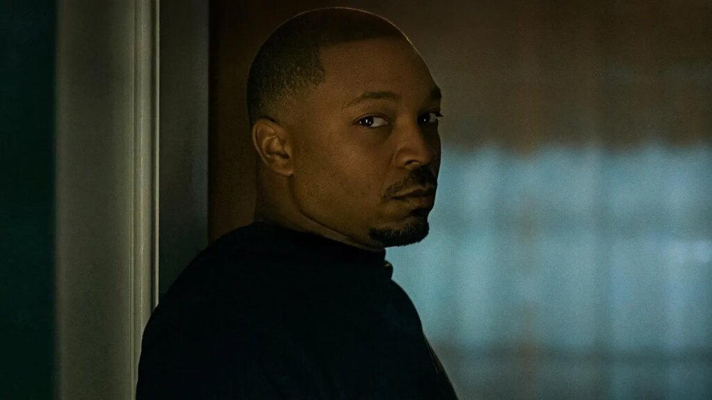Malcolm Mays as Lou in Raising Kanan leans against wall while staring into a room.