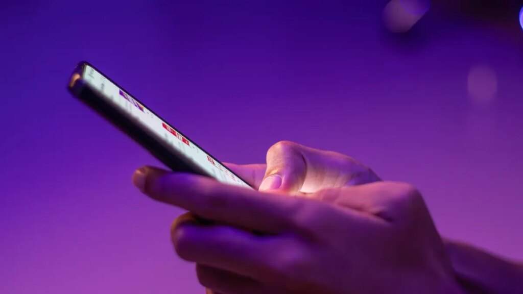 Hackers Conned a Chatbot to Hijack 20,000 Instagram Accounts A closeup of a person's hands typing a message on smartphone in dark room with neon purple light.