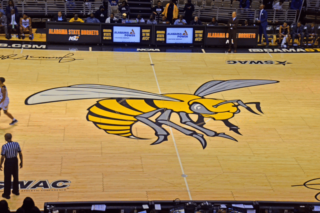 NCAA details Alabama State betting scheme Wide view of Alabama State Hornets basketball court featuring the large hornet logo at center court, linked to NCAA findings involving former Alabama State players in the Southern Mississippi betting manipulation investigation.