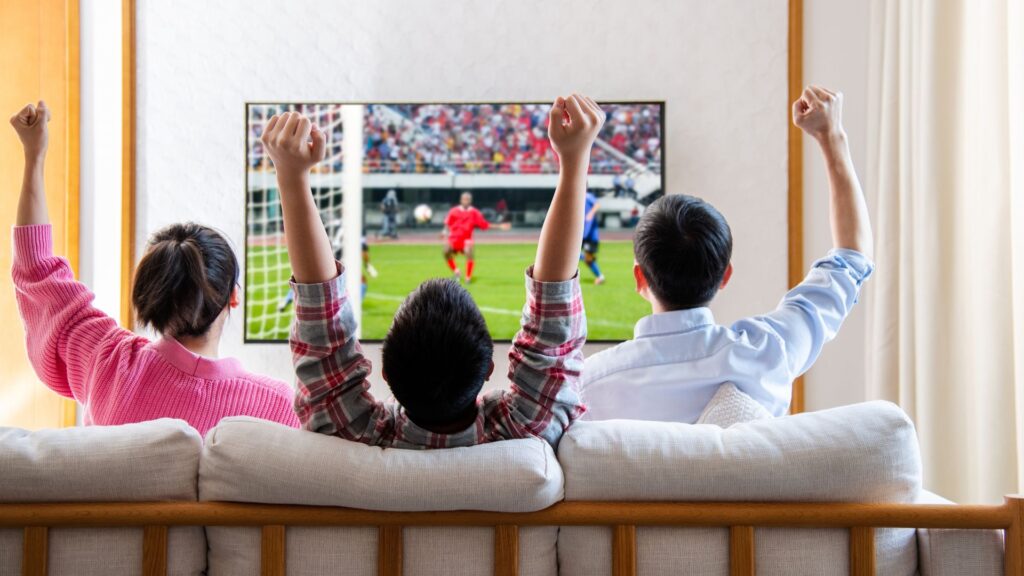 This is the cheapest way to stream every World Cup match in 2026 — but there’s a catch Family watching television and cheering soccer game on TV together in their living room.