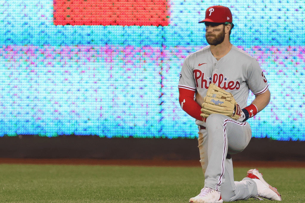 Bryce Harper of the Philadelphia Phillies kneels on the field before an MLB game amid FanDuel Cameo gambling promotion controversy.